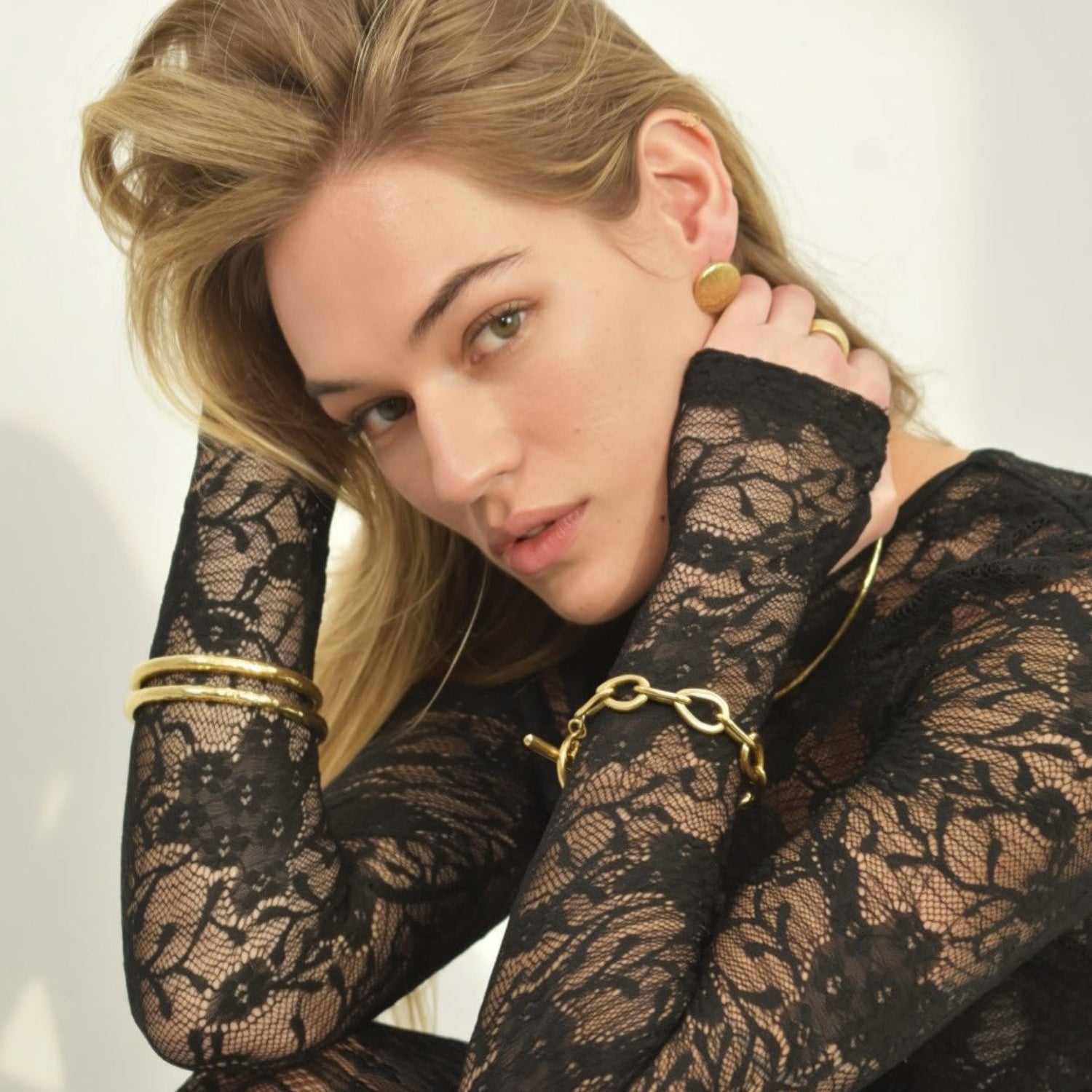 Woman wearing black lace gloves and gold jewelry against a white background