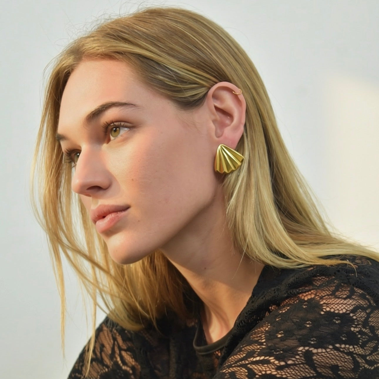 Woman wearing gold shell earrings with a neutral background