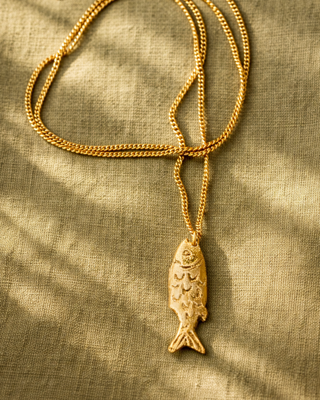 Gold fish pendant necklace on a textured beige fabric background